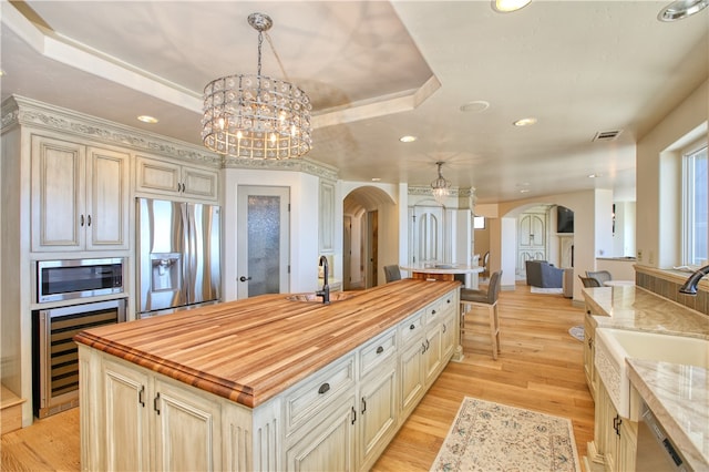 kitchen featuring an island with sink, beverage cooler, hanging light fixtures, light hardwood / wood-style flooring, and appliances with stainless steel finishes