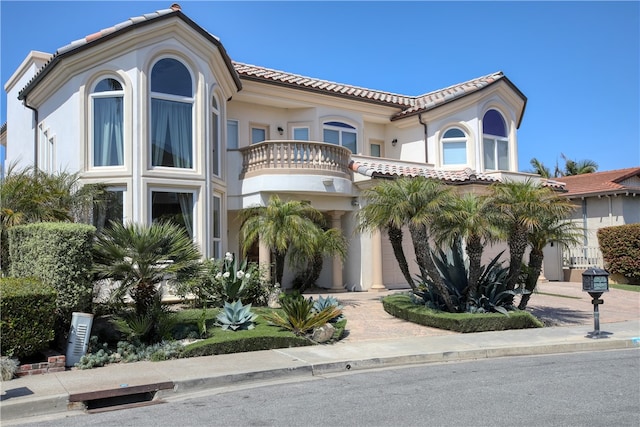 mediterranean / spanish-style home with a tiled roof, decorative driveway, a balcony, and stucco siding