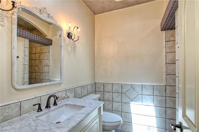 bathroom with toilet, vanity, wainscoting, and tile walls
