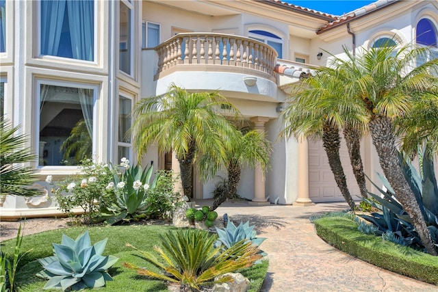 doorway to property with a balcony, a garage, a tile roof, decorative driveway, and stucco siding