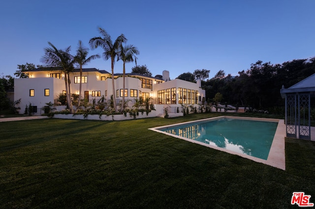 pool at dusk featuring a lawn