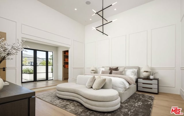 bedroom with a high ceiling, french doors, access to outside, light hardwood / wood-style floors, and a chandelier