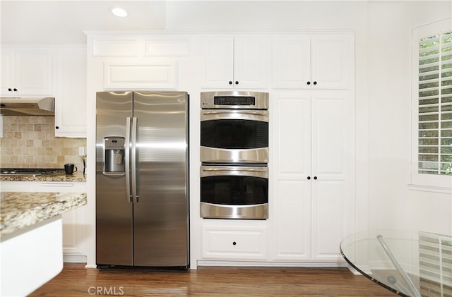 kitchen featuring light stone counters, dark hardwood / wood-style floors, ventilation hood, white cabinets, and stainless steel appliances