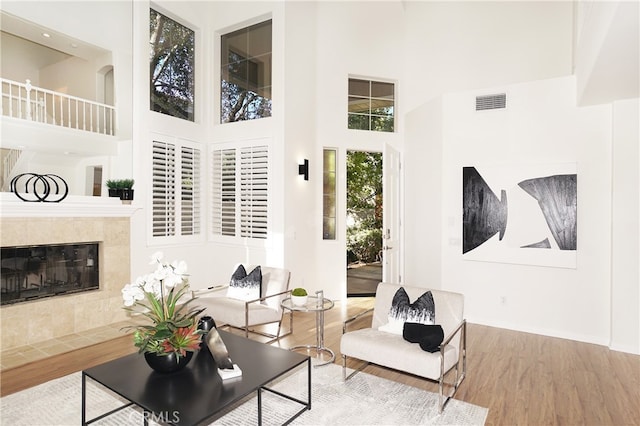 living room featuring a tile fireplace, a towering ceiling, and wood-type flooring