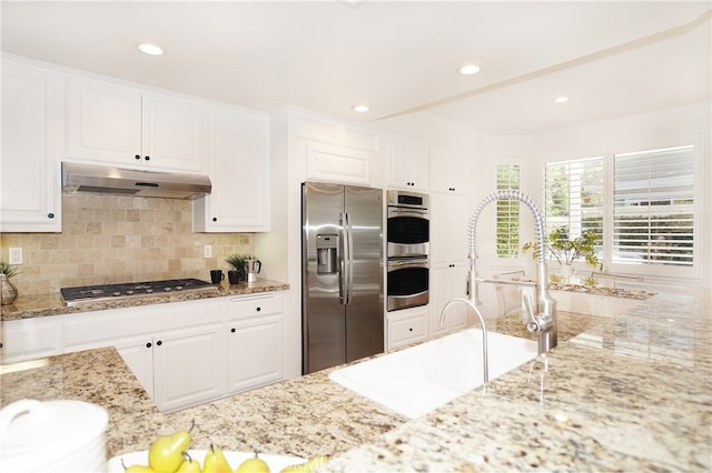 kitchen with light stone counters, sink, backsplash, white cabinetry, and appliances with stainless steel finishes