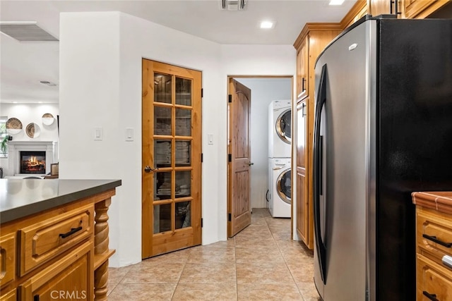 kitchen featuring stainless steel fridge, stacked washer and clothes dryer, and light tile patterned floors