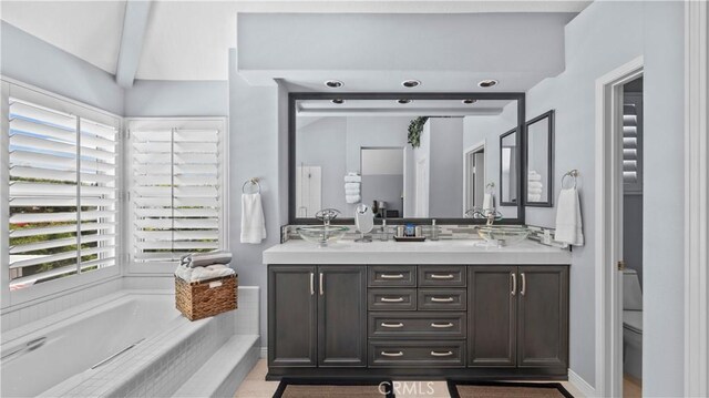 bathroom featuring beamed ceiling, vanity, tiled bath, and plenty of natural light