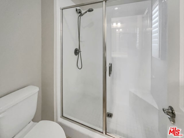 bathroom featuring a shower with shower door and toilet