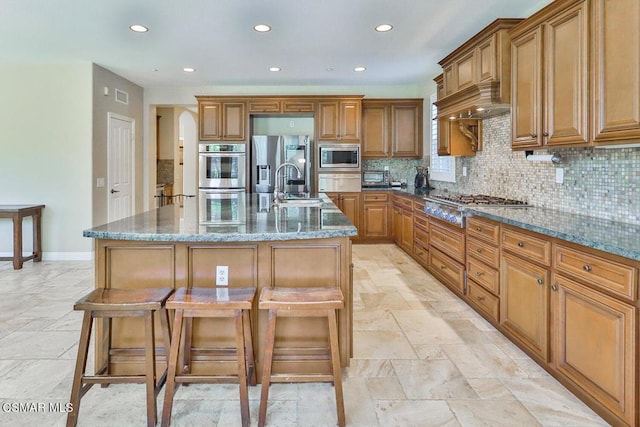 kitchen featuring a kitchen bar, stainless steel appliances, sink, a center island with sink, and stone counters