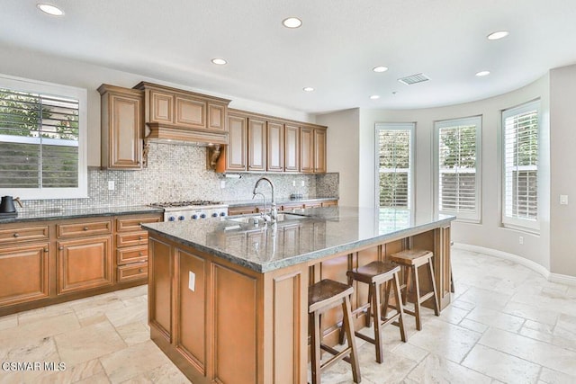 kitchen with a breakfast bar area, backsplash, a kitchen island with sink, and dark stone counters