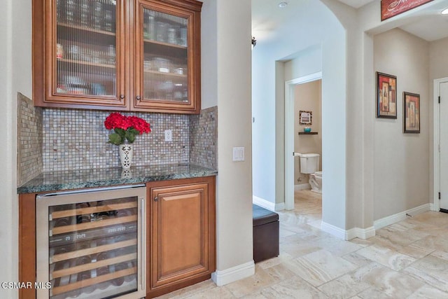 bar with tasteful backsplash, dark stone countertops, and beverage cooler