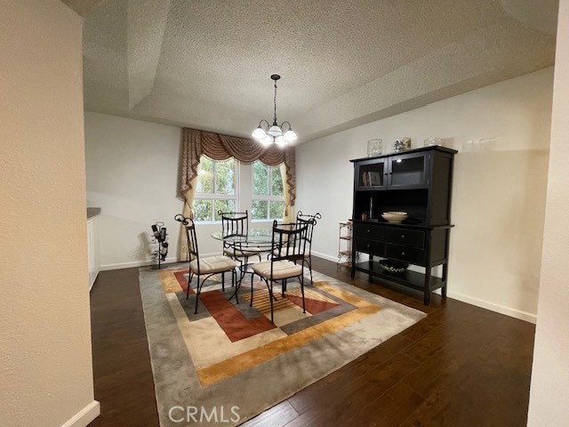 dining area with a textured ceiling, a notable chandelier, and dark hardwood / wood-style flooring