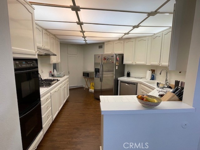 kitchen with sink, kitchen peninsula, white cabinetry, appliances with stainless steel finishes, and dark hardwood / wood-style flooring