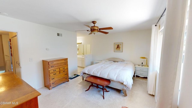 bedroom featuring light carpet, ensuite bathroom, and ceiling fan