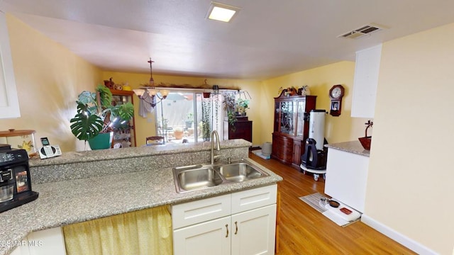 kitchen with white cabinets, sink, light stone countertops, light hardwood / wood-style floors, and a chandelier