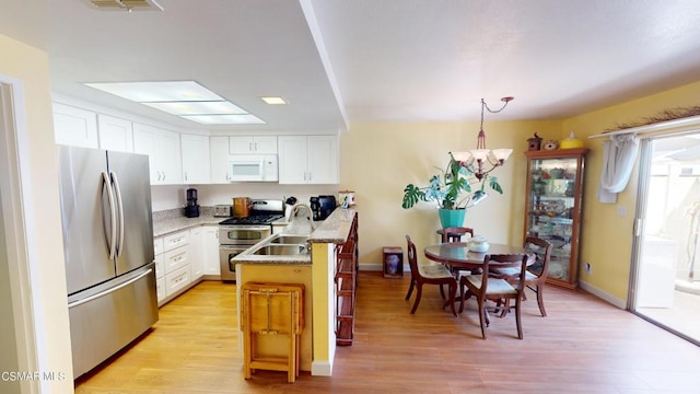 kitchen with kitchen peninsula, appliances with stainless steel finishes, light wood-type flooring, decorative light fixtures, and white cabinets