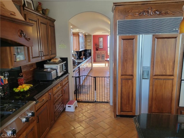 34135 Cameron Dr, Sage, CA 92544 - kitchen with dark countertops, arched walkways, brick floor, brown cabinetry, and appliances with stainless steel finishes