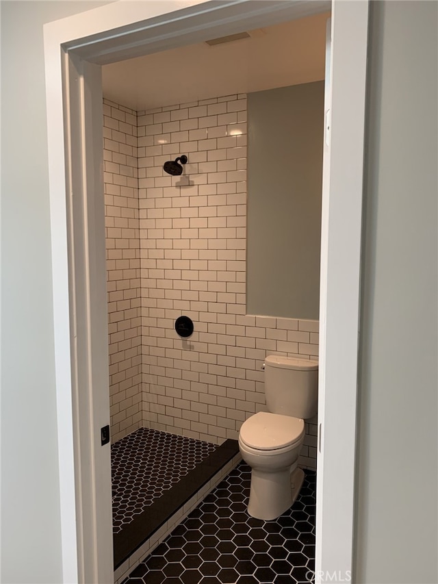 bathroom with tiled shower, tile patterned flooring, toilet, and tile walls