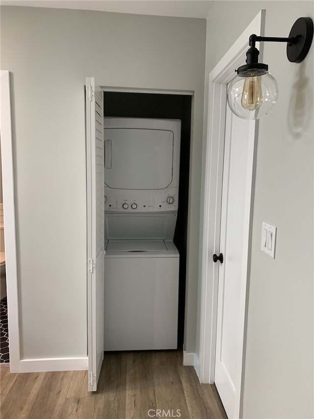 clothes washing area with stacked washer and dryer and wood-type flooring