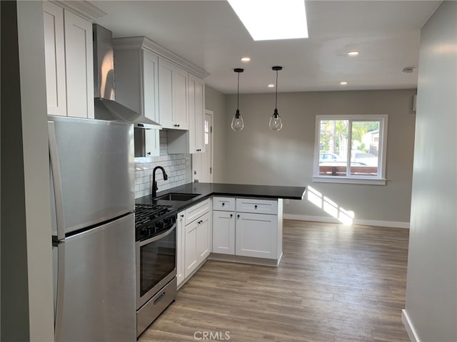 kitchen featuring white cabinetry, sink, wall chimney range hood, decorative light fixtures, and appliances with stainless steel finishes