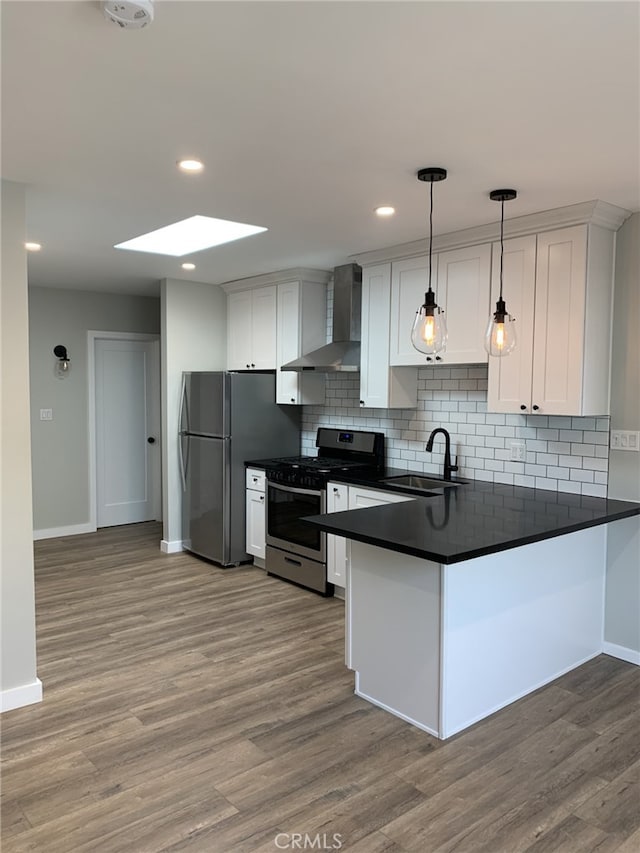 kitchen featuring wall chimney range hood, sink, hanging light fixtures, white cabinetry, and stainless steel appliances