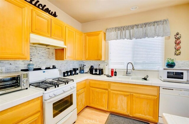 kitchen featuring white appliances, sink, light hardwood / wood-style floors, tile counters, and decorative backsplash