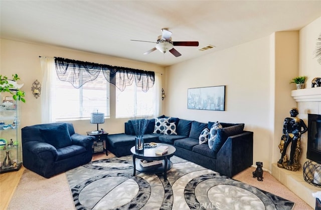 living room featuring a tiled fireplace, wood-type flooring, and ceiling fan