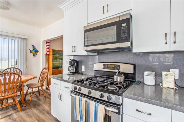 kitchen with appliances with stainless steel finishes, light hardwood / wood-style floors, white cabinets, and tasteful backsplash