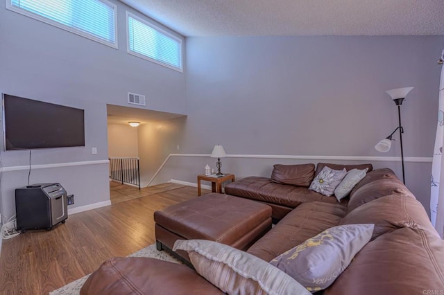 living room featuring wood-type flooring, high vaulted ceiling, and a textured ceiling