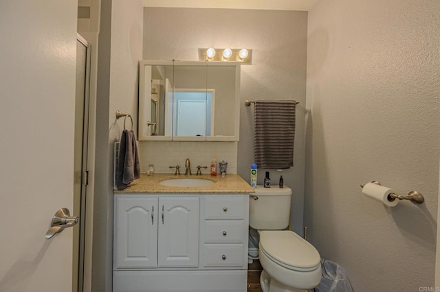 bathroom featuring vanity, backsplash, toilet, and a shower with shower door