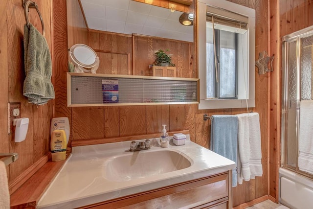 bathroom featuring wooden walls, vanity, and bath / shower combo with glass door