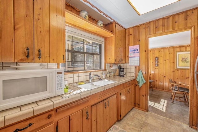 kitchen with decorative backsplash, tile counters, wood walls, and sink