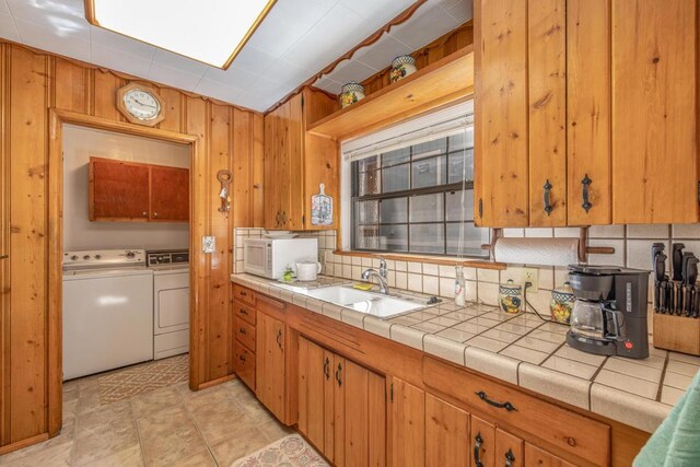 kitchen with backsplash, washer and clothes dryer, sink, tile countertops, and wood walls