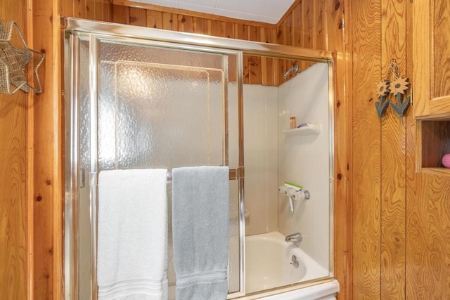 bathroom with wood walls and combined bath / shower with glass door