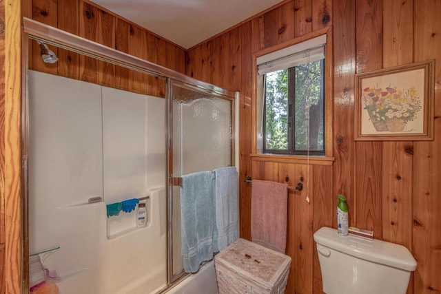 bathroom with toilet, shower / bath combination with glass door, and wooden walls