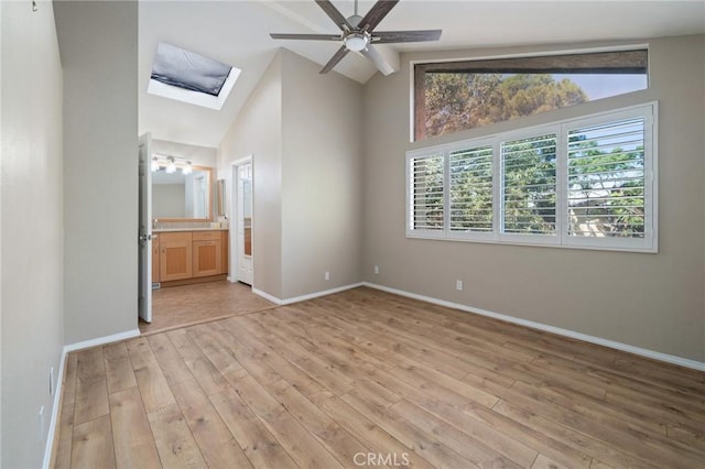 unfurnished bedroom featuring connected bathroom, light hardwood / wood-style floors, lofted ceiling with skylight, and ceiling fan