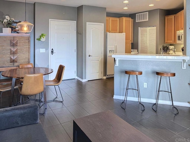 kitchen with a peninsula, light brown cabinetry, visible vents, a kitchen bar, and white appliances