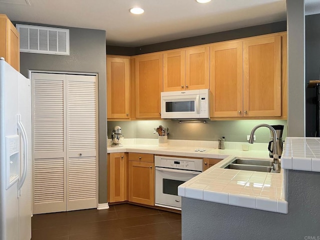 kitchen with tile counters, a sink, light brown cabinetry, white appliances, and visible vents