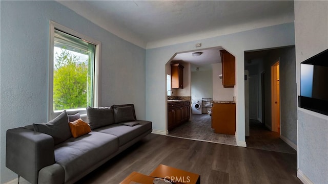 living area with arched walkways, baseboards, washer / dryer, dark wood-style flooring, and a textured wall