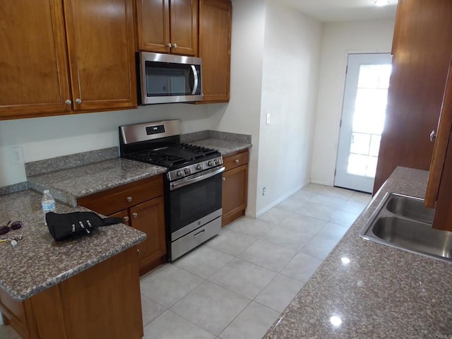 kitchen featuring dark stone countertops, sink, light tile patterned floors, and stainless steel appliances