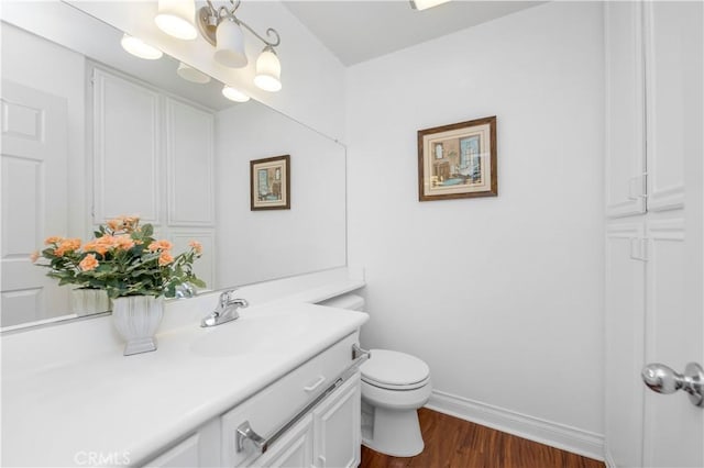 bathroom featuring toilet, vanity, baseboards, and wood finished floors