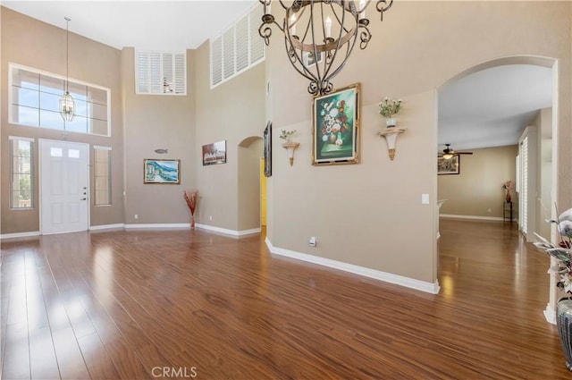 foyer entrance with baseboards, visible vents, arched walkways, dark wood finished floors, and a high ceiling