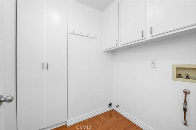 clothes washing area featuring hookup for a washing machine, cabinets, and light hardwood / wood-style floors