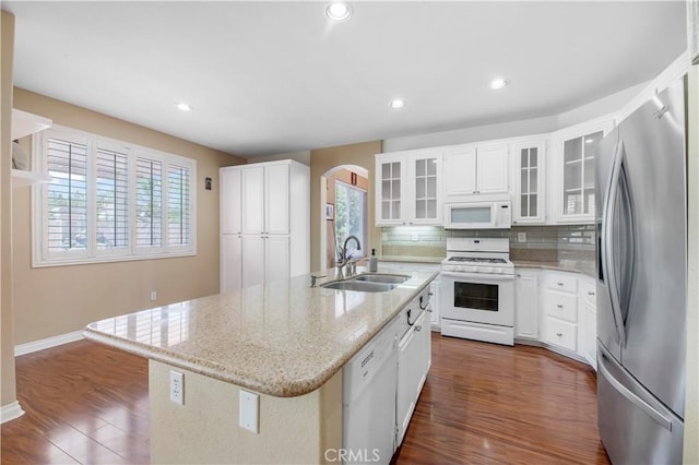 kitchen featuring arched walkways, a kitchen island with sink, white appliances, a sink, and decorative backsplash