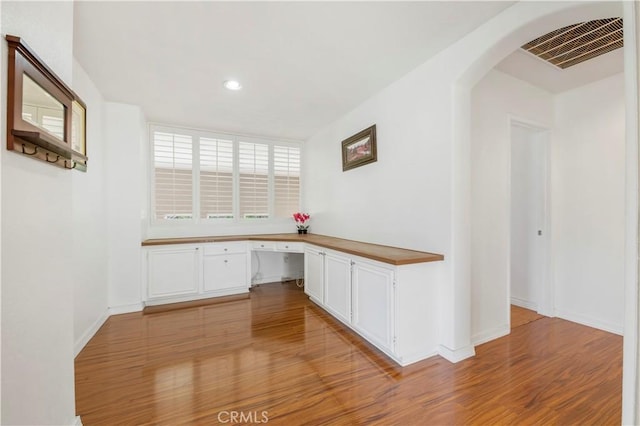 unfurnished office featuring arched walkways, light wood-style flooring, recessed lighting, visible vents, and built in study area