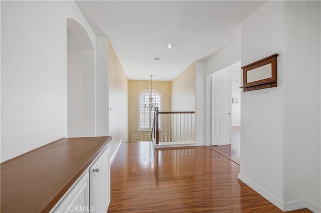 hall featuring a chandelier, wood finished floors, and baseboards