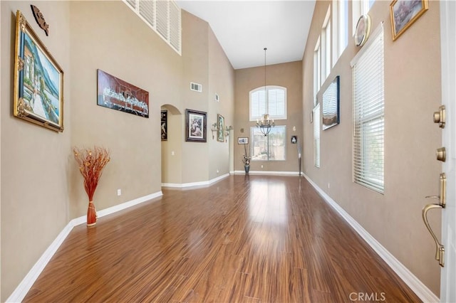 foyer entrance with baseboards, visible vents, arched walkways, and wood finished floors