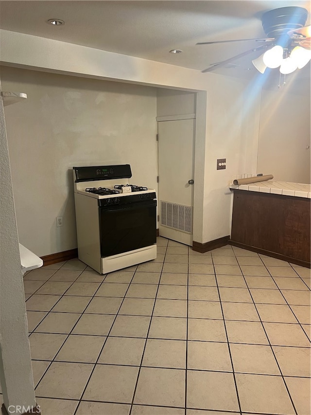 kitchen featuring dark brown cabinets, white gas range oven, tile counters, light tile patterned floors, and ceiling fan