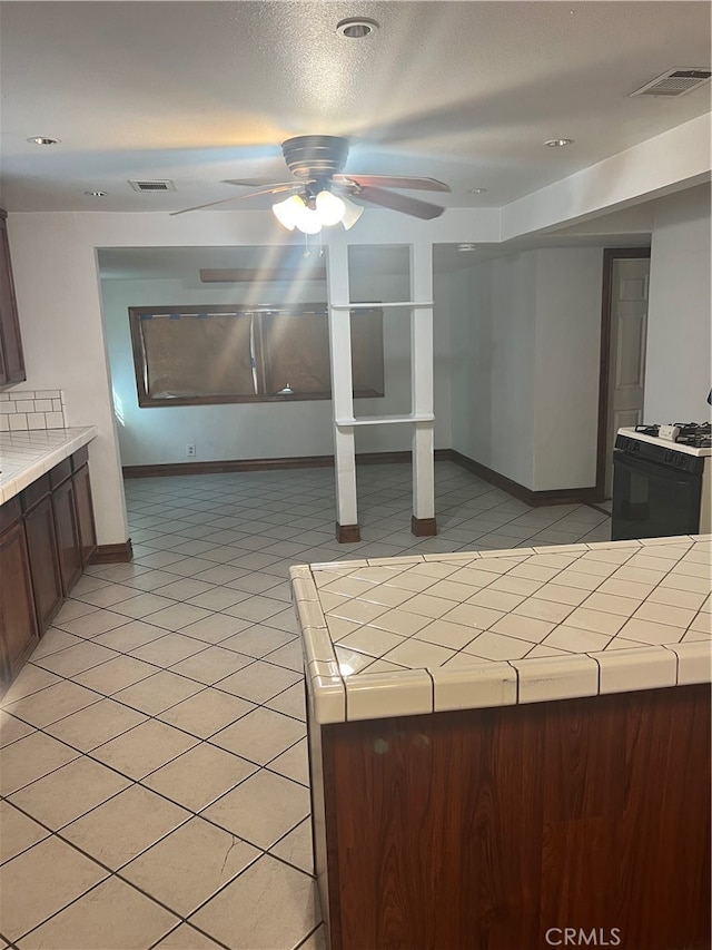 interior space with ceiling fan, light tile patterned floors, tile counters, and white gas range