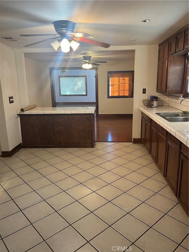 kitchen featuring tasteful backsplash, sink, tile countertops, dark brown cabinetry, and ceiling fan